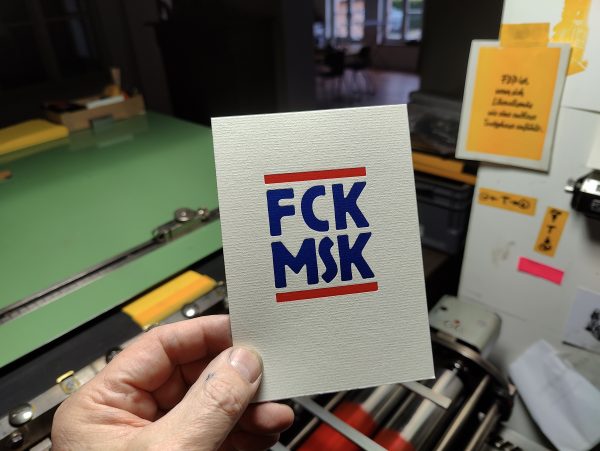 Hand hält FCK MSK Karte vor Druckmaschine.