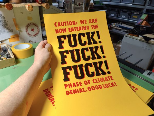 Hand hält gelbes Plakat in rot und schwarz auf dem steht: Caution: We are Not entring the FUCK! FUCK! FUCK! Phase of climate denial. Good Luck!