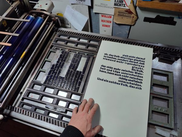 Foto Abzug des ersten Teils der dreiteiligen Bleisatzarbeit auf der Druckmaschine neben der Druckform. Meine Hand als Größenhinweis im Bild. Der Druck wird etwa drei Handlängen hoch.