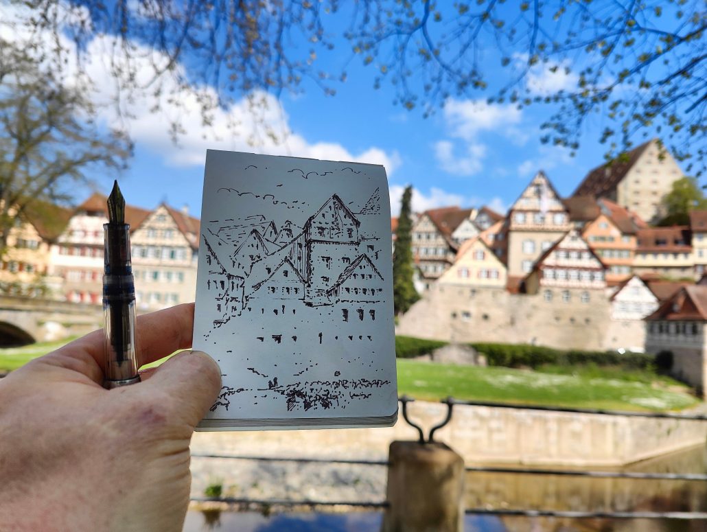 Foto Hand hält Skizzenbuch mit Füllerzeichnung des mittalterlichen Teiles von Schwäbisch Hall vor das Motiv