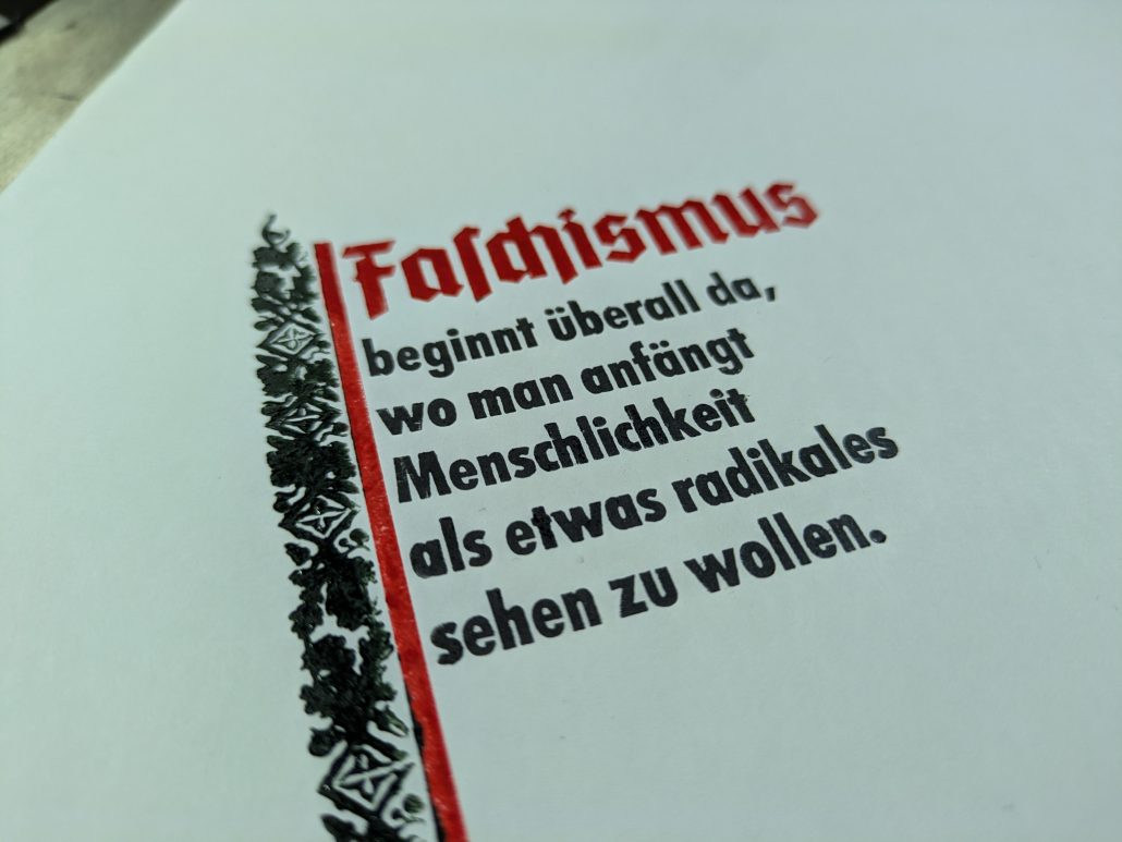 Detailfoto eines dreifarbigen Probedrucks. Der fahnenartige Text liest sich: Faschismus beginnt überall da, wo man beginnt Menschlichkeit als etwas Radikales sehen zu wollen.