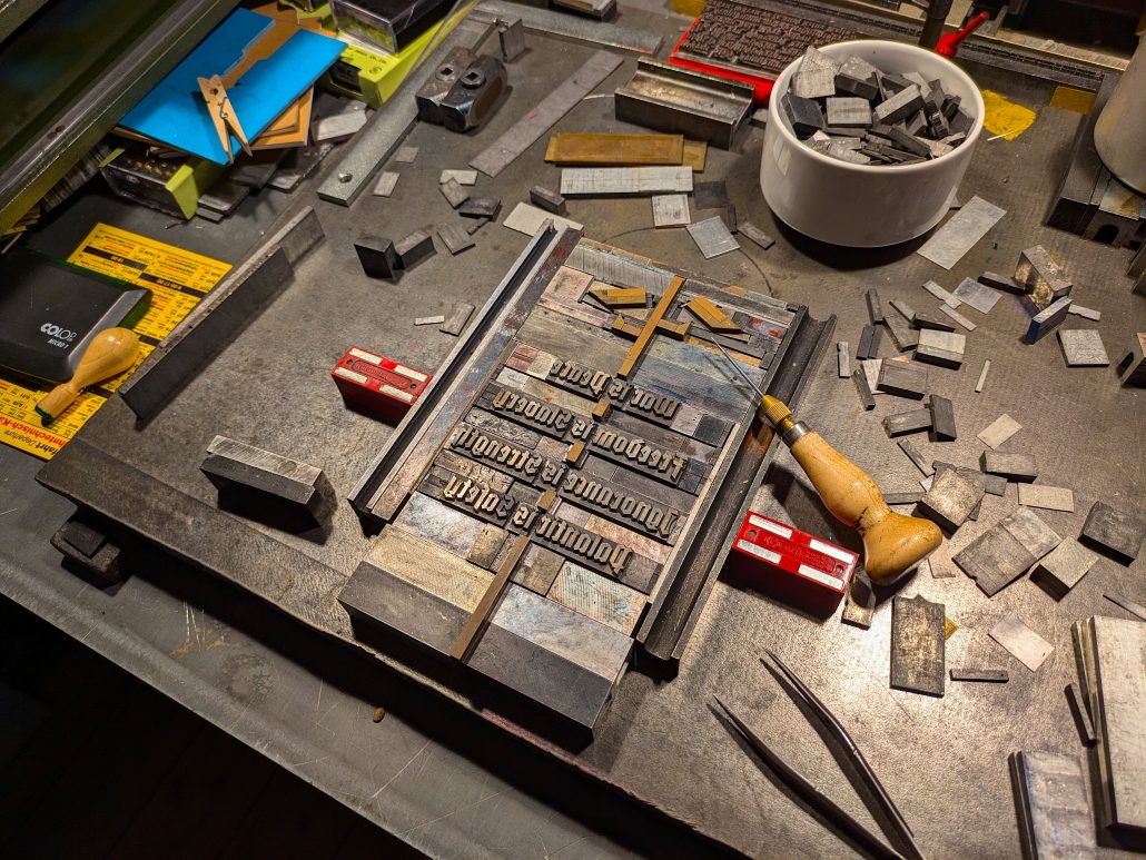 Foto der Arbeitssituation der Bleisatzform fertig zum Ausbinden und Transportieren zur Druckmaschine auf dem Schließtisch mit Werkzeug und Blindmaterial. 