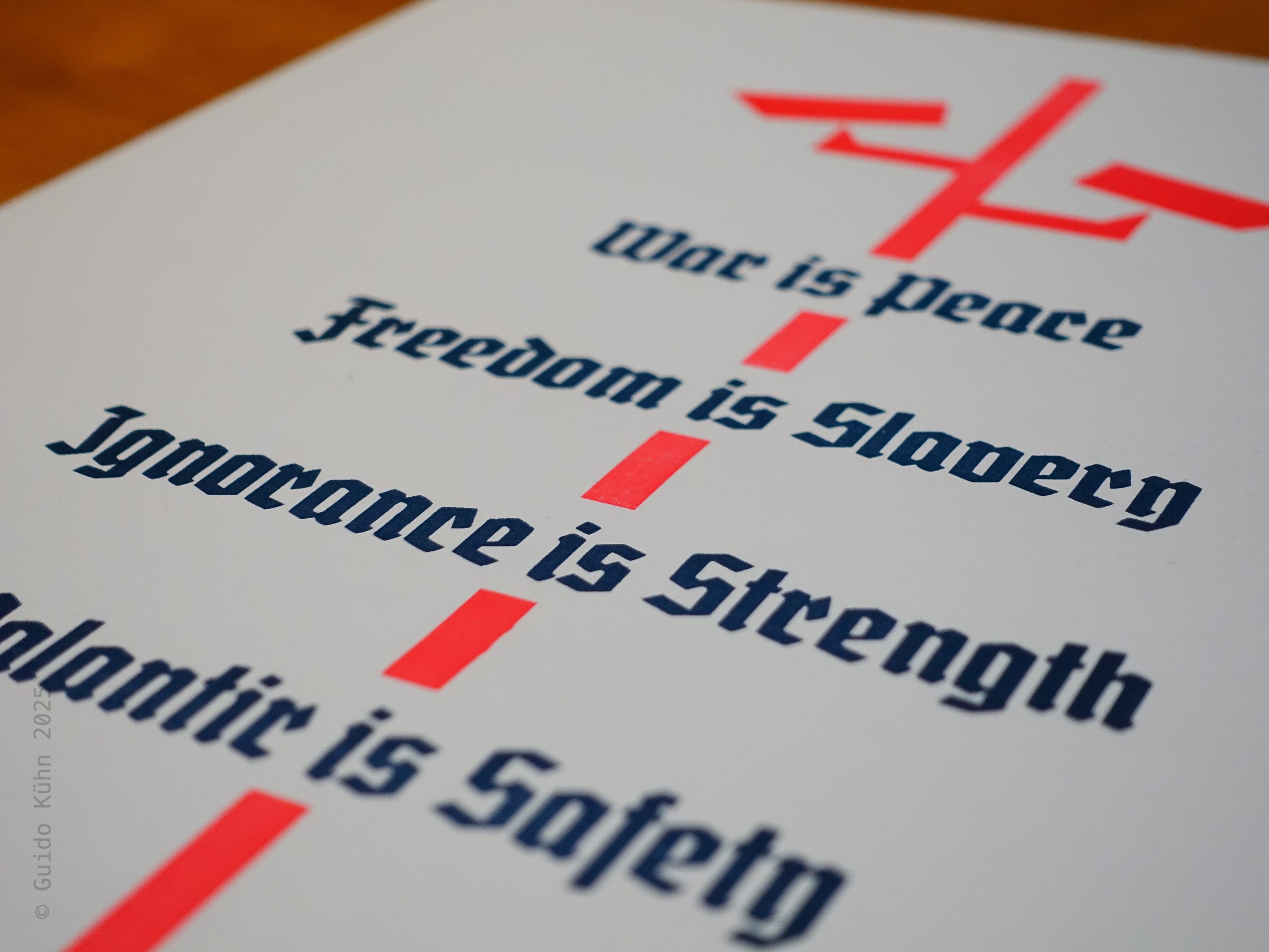 Foto eines zweifarbigen Abzugs mit einem stilisierten Mast, auf dem Überwachungskameras in leuchtendem Rot angebracht sind. Durchbrochen wird das Bild von den in Blauschwarz gehaltenen, aus George Orwells „1984” zitierten Zeilen „War is Peace, Freedom is Slavery, Ignorance is Strength”. Ich habe die Zeilen um die Zeile „Palantir is Safety” ergänzt.