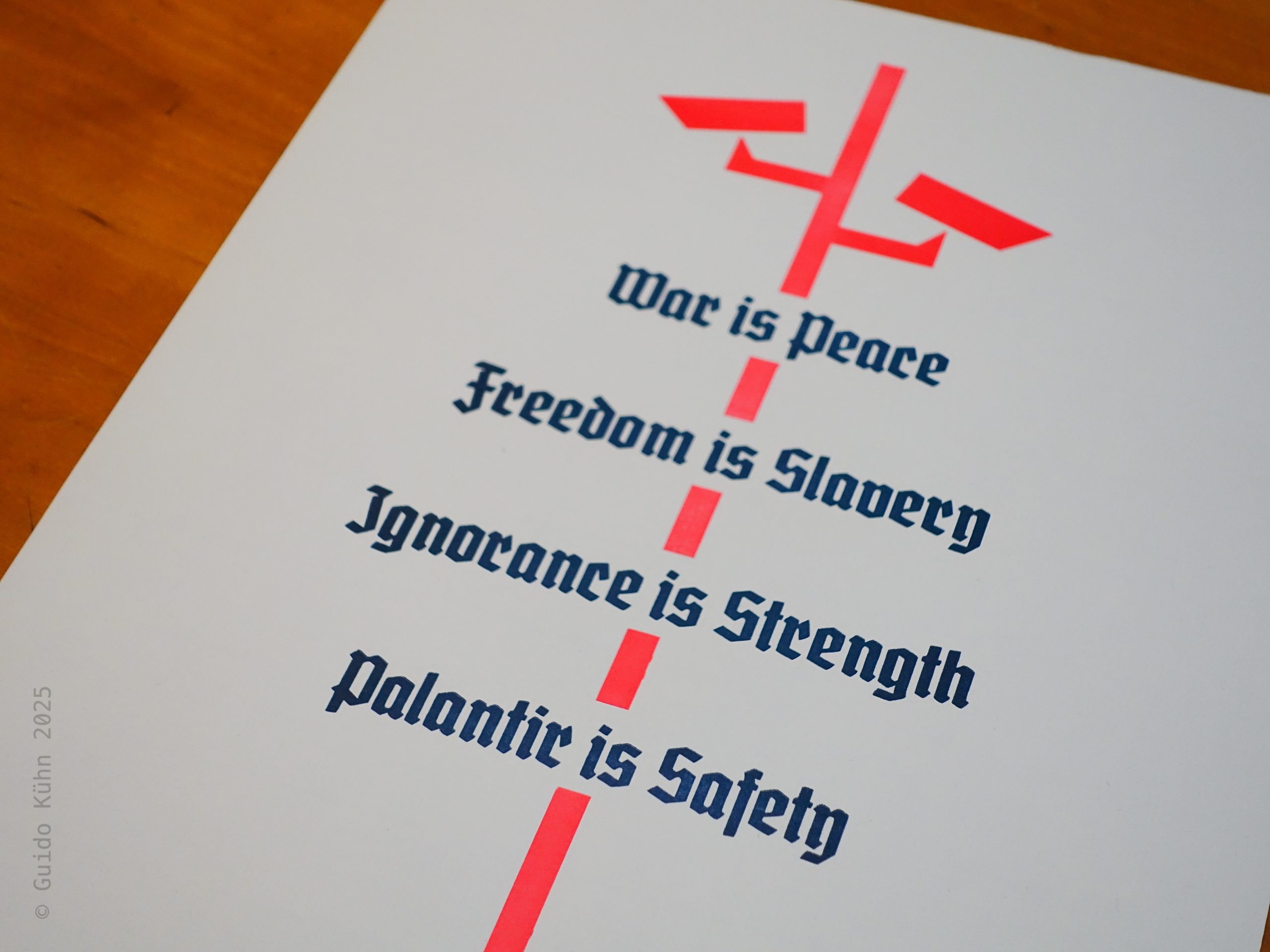 Foto eines zweifarbigen Abzugs mit einem stilisierten Mast, auf dem Überwachungskameras in leuchtendem Rot angebracht sind. Durchbrochen wird das Bild von den in Blauschwarz gehaltenen, aus George Orwells „1984” zitierten Zeilen „War is Peace, Freedom is Slavery, Ignorance is Strength”. Ich habe die Zeilen um die Zeile „Palantir is Safety” ergänzt.