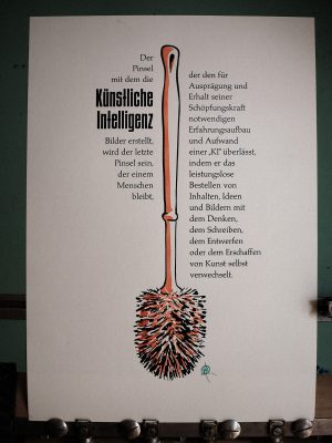 Foto mit dem fertigen Abzug. Man sieht einen Formtext um eine Klobürste. Der Text lautet: Der Pinsel mit dem die Künstliche Intelligenz Bilder erstellt, wird der letzte Pinsel sein, der einem Menschen bleibt, der den für Ausprägung und Erhalt seiner Schöpfungskraft notwendigen Erfahrungsaufbau und Aufwand einer „KI“ überlässt, indem er das leistungslose Bestellen von Inhalten, Ideen und Bildern mit dem Denken, dem Schreiben, dem Entwerfen oder dem Erschaffen von Kunst verwechselt.